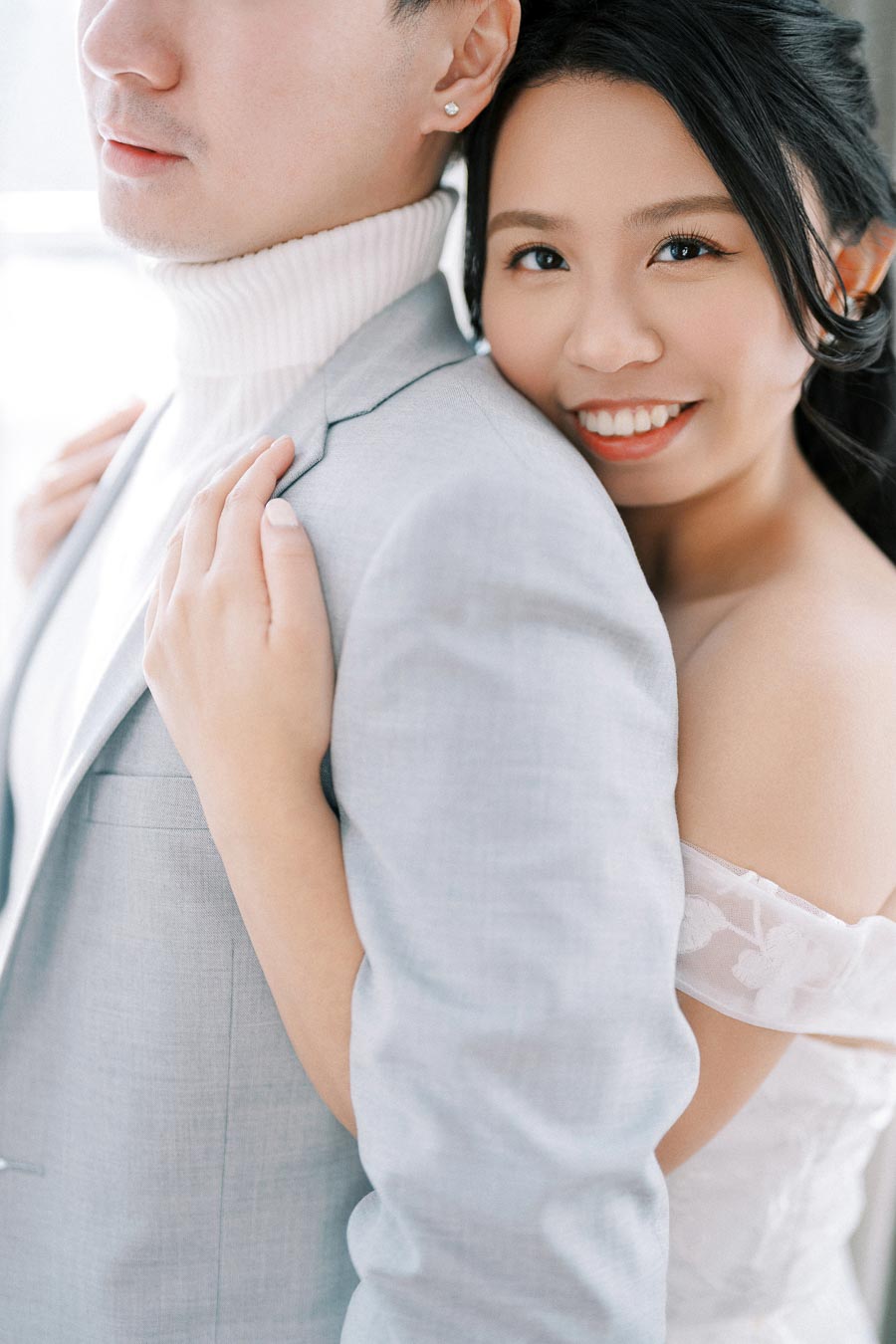 Smiling woman embracing partner in elegant attire, showcasing joyful affection in a romantic setting.