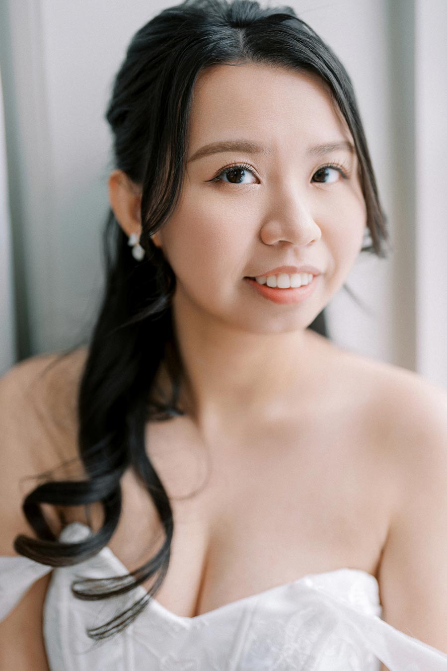 A woman with long dark hair smiles softly while wearing a white strapless dress.