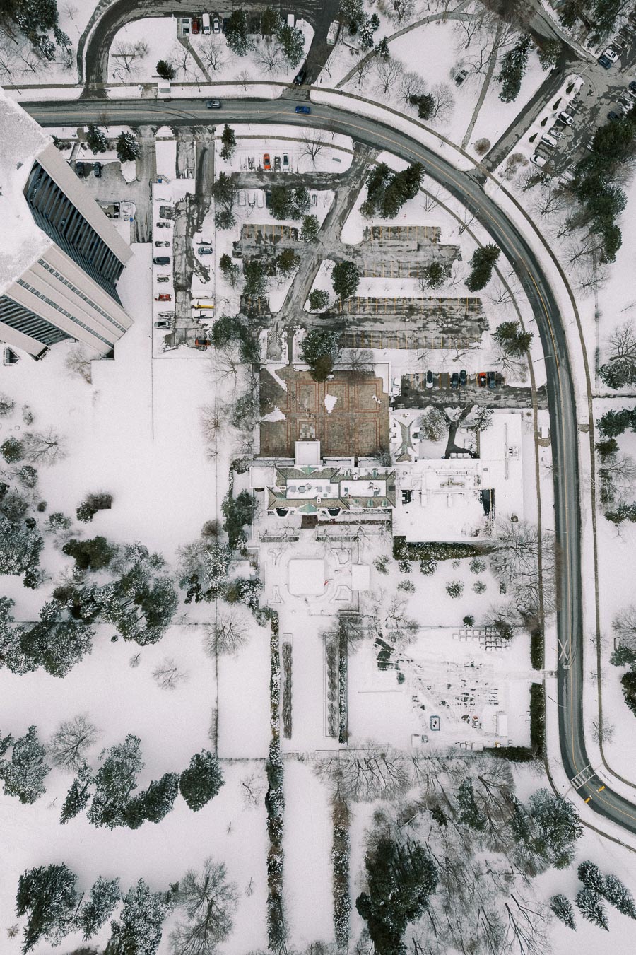 Arial view of a snow-covered urban landscape featuring roads, trees, and high-rise buildings.