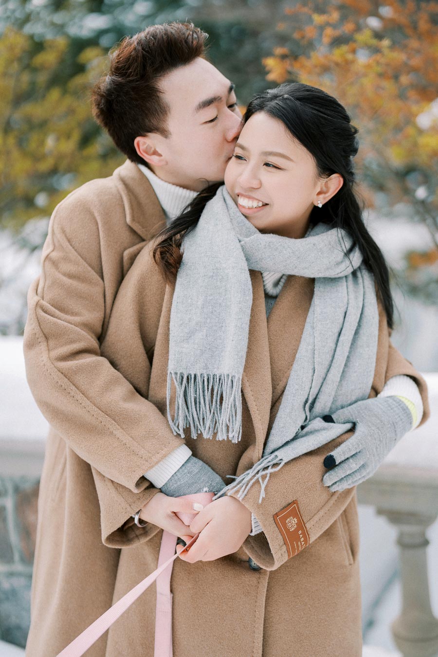 Young couple in winter clothing embracing outdoors, enjoying a snowy day.