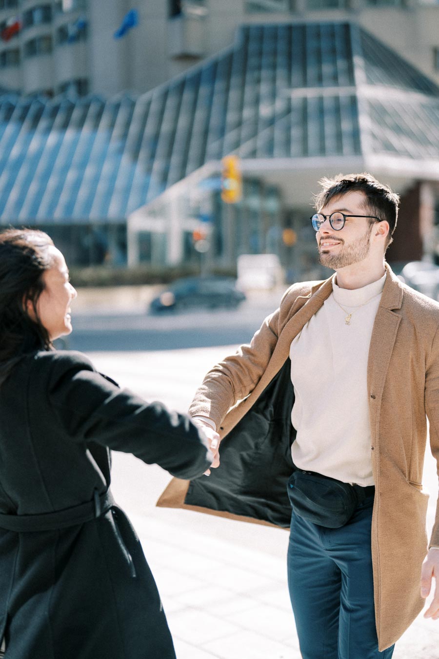 Two individuals greet each other with a handshake on a sunny day in the city, with a modern glass building in the background.