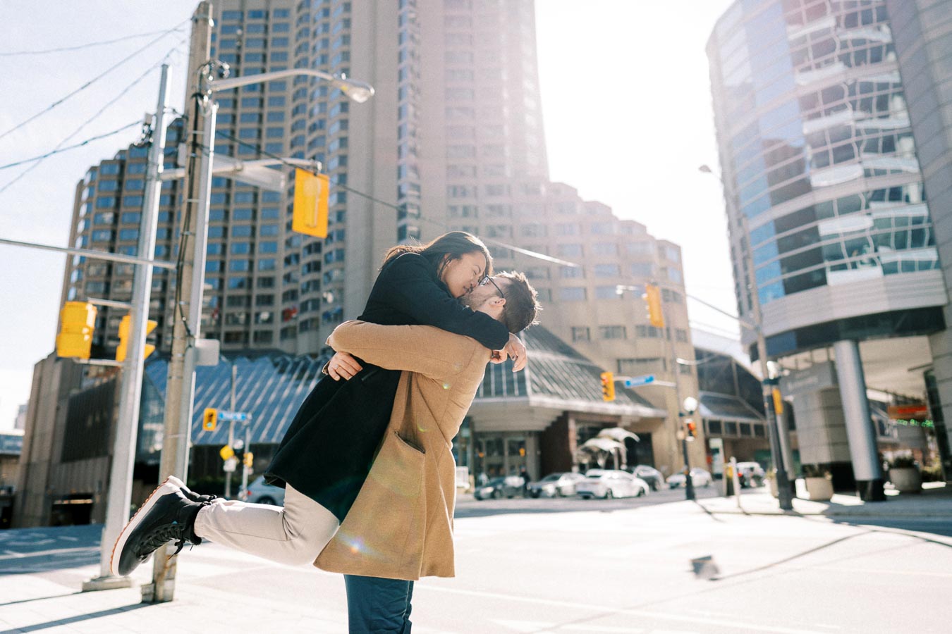 A couple shares a romantic moment on a city street, surrounded by tall buildings and urban architecture.