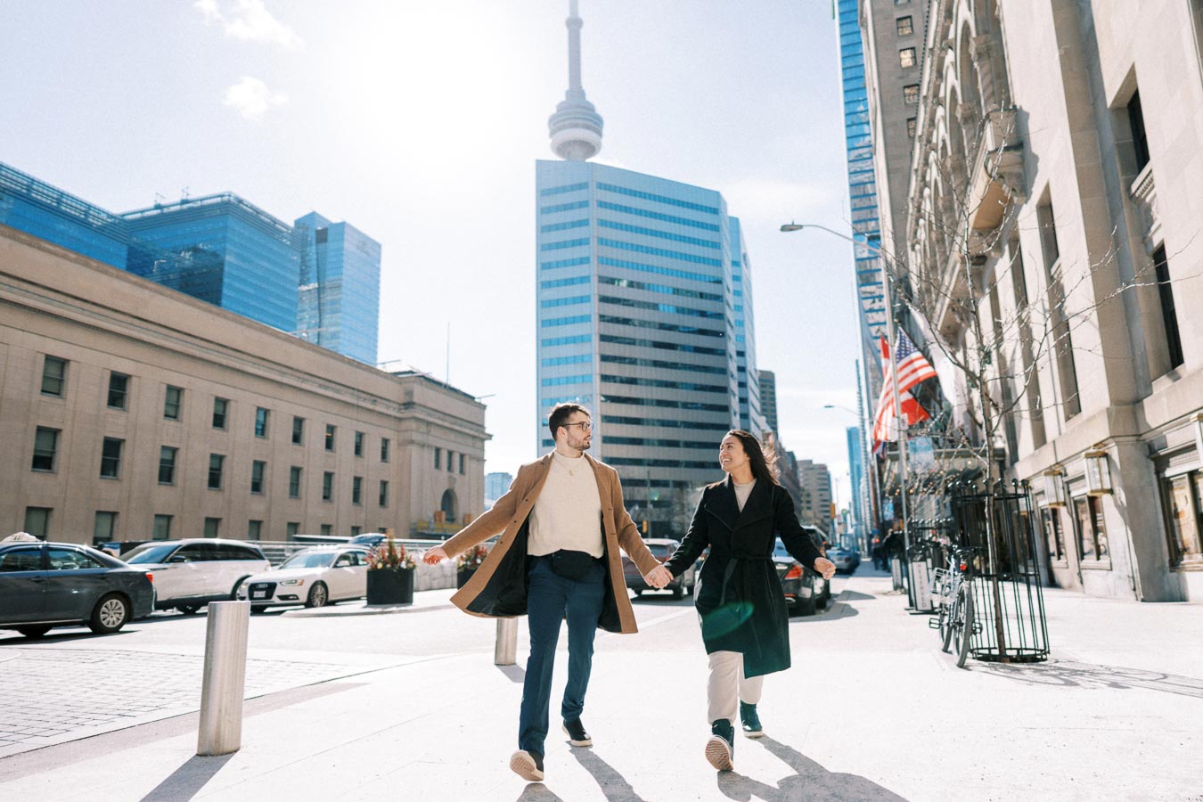 A couple enjoys a sunny day in Toronto, walking hand in hand with the iconic CN Tower in the background.