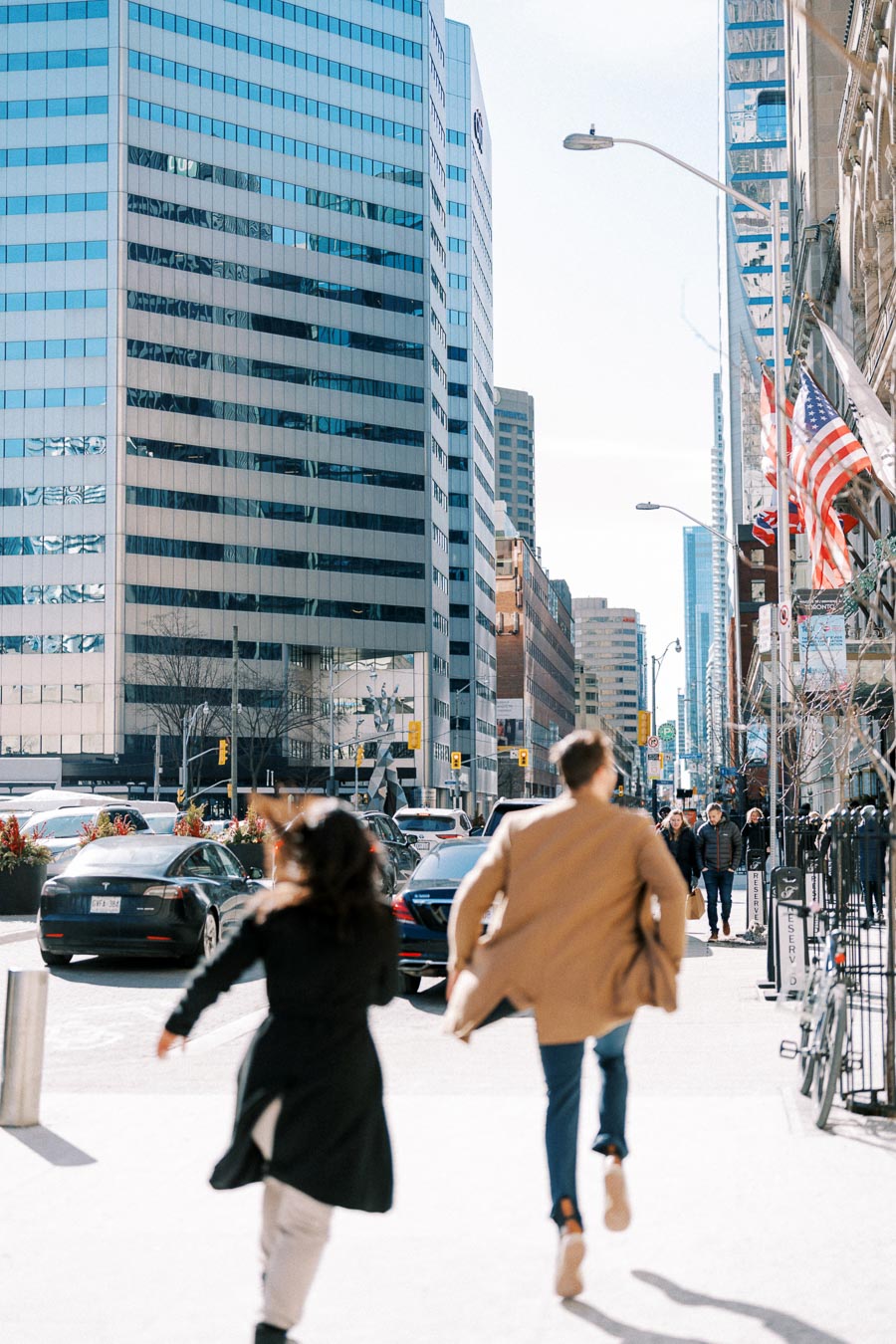 A bustling city street scene with people walking, surrounded by tall modern buildings and American flags.