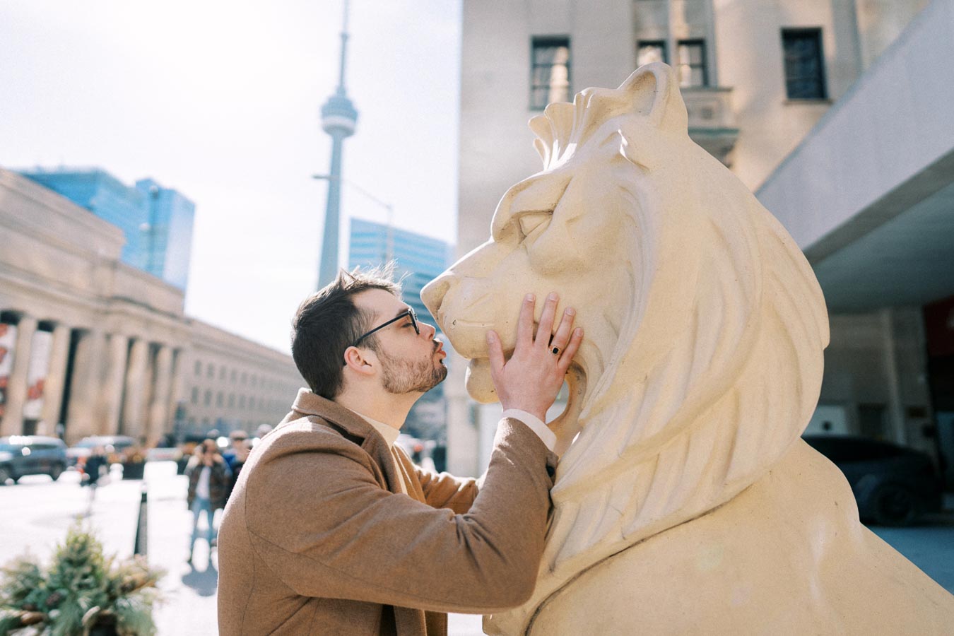 A man playfully kisses a lion statue in front of the CN Tower in Toronto.