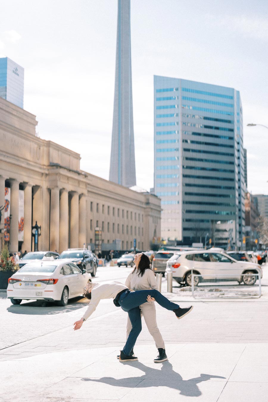 A playful moment captured in front of the CN Tower in Toronto, featuring two people enjoying a lighthearted interaction amidst the urban backdrop.