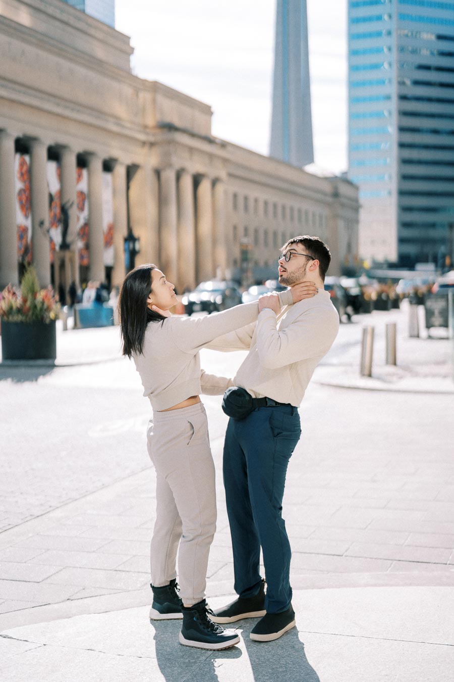 A playful moment between two people in an urban setting, with a prominent tower and classical architecture in the background.