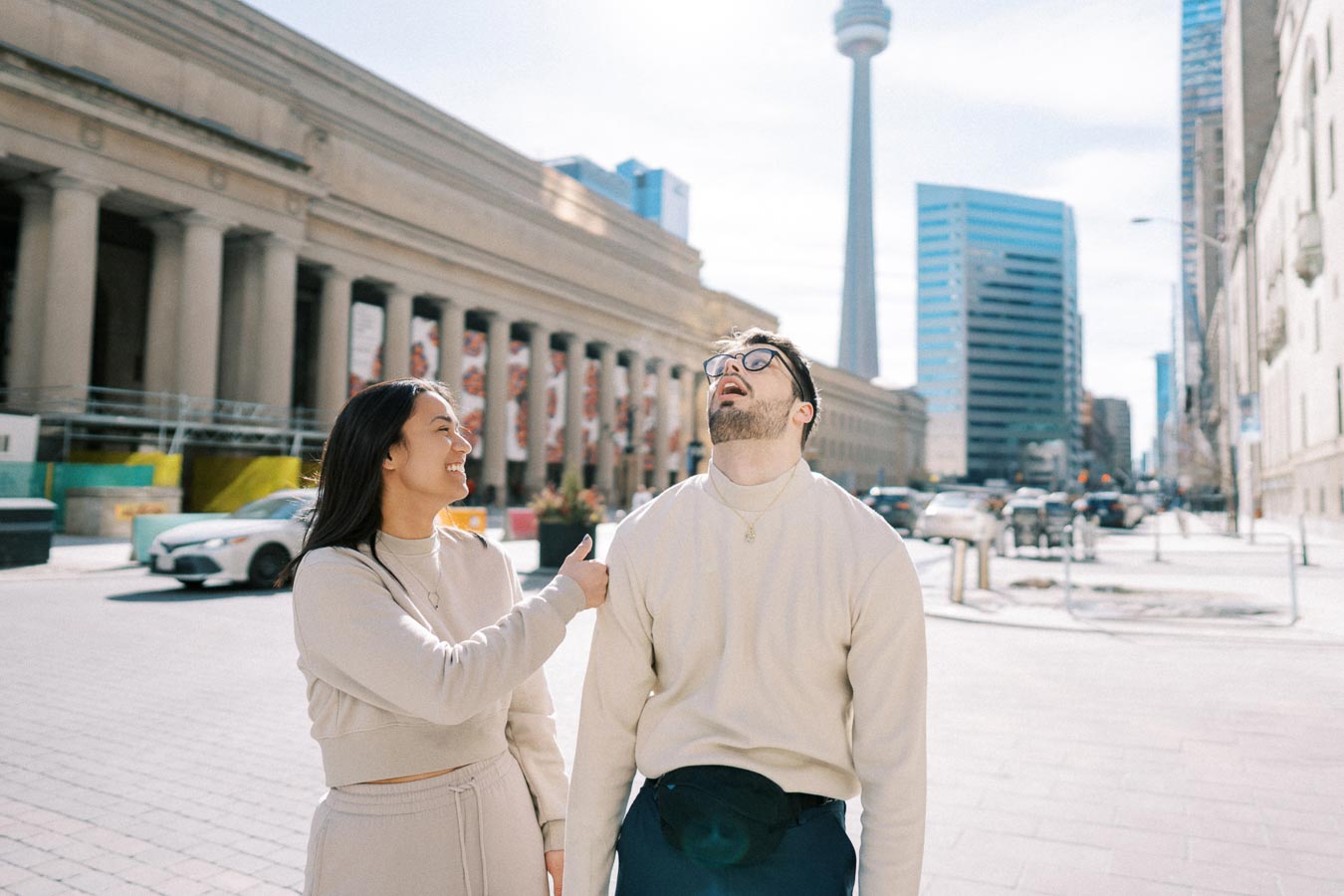 A joyful moment captured between two people in front of a historic building in Toronto, with the CN Tower in the background.