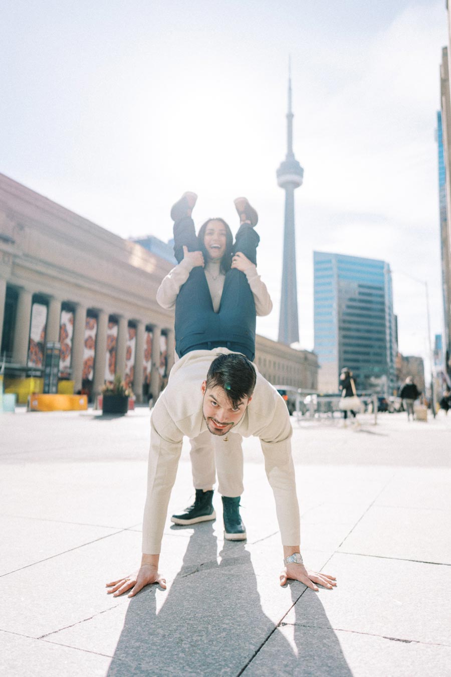 A playful moment captured in front of the CN Tower in Toronto, featuring a couple enjoying a fun pose.