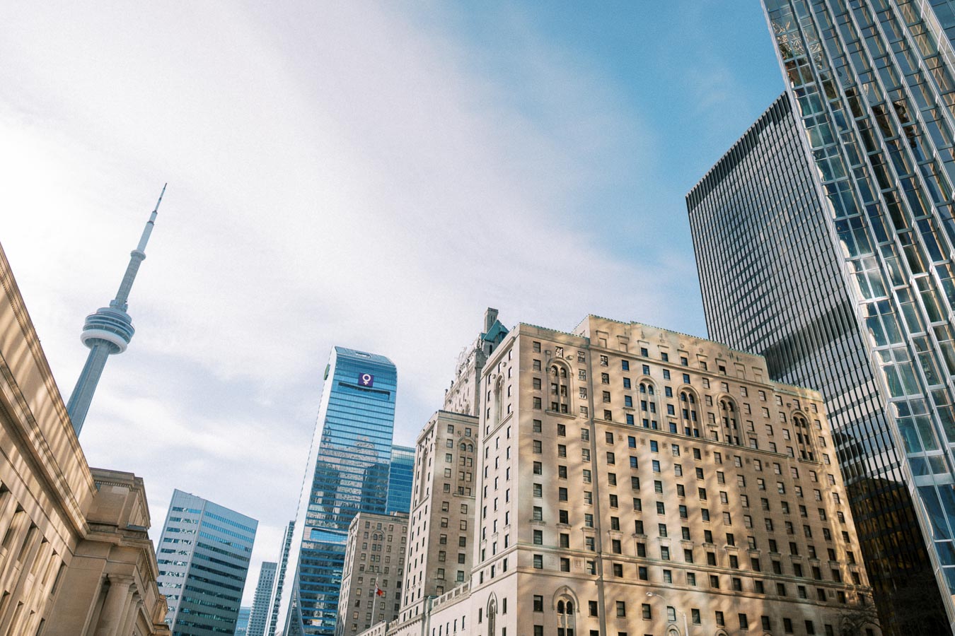 A view of Toronto's skyline showcasing the iconic CN Tower alongside modern and historic buildings under a clear blue sky.