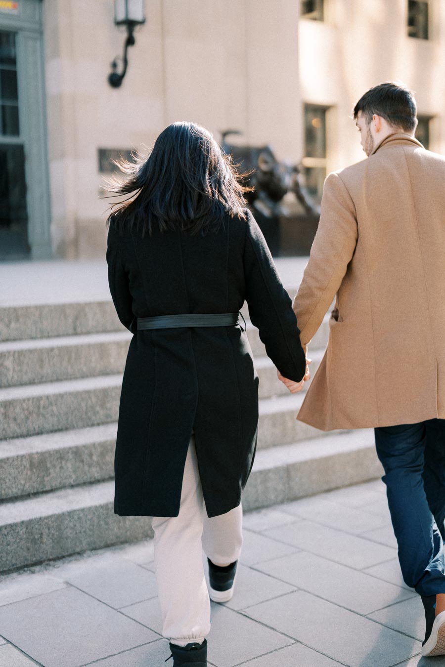 A couple walks hand in hand up the steps, dressed warmly in winter coats.
