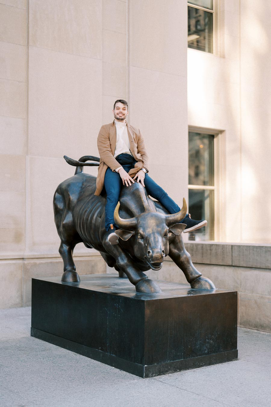 A person sits atop the famous Charging Bull statue located in the Financial District of New York City, symbolizing financial optimism and prosperity.