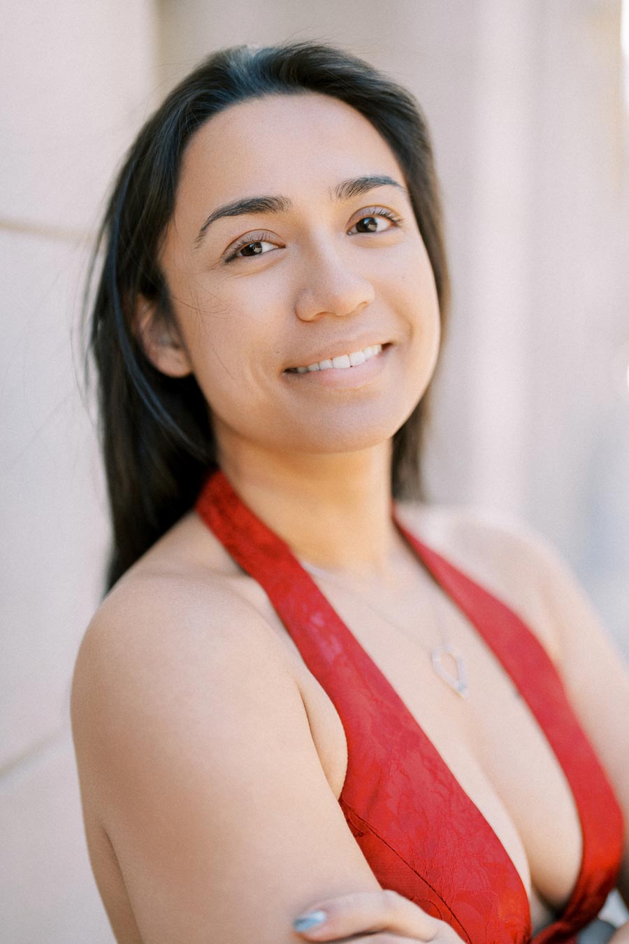 A woman in a red halter top smiles warmly at the camera, showcasing her heart-shaped necklace.