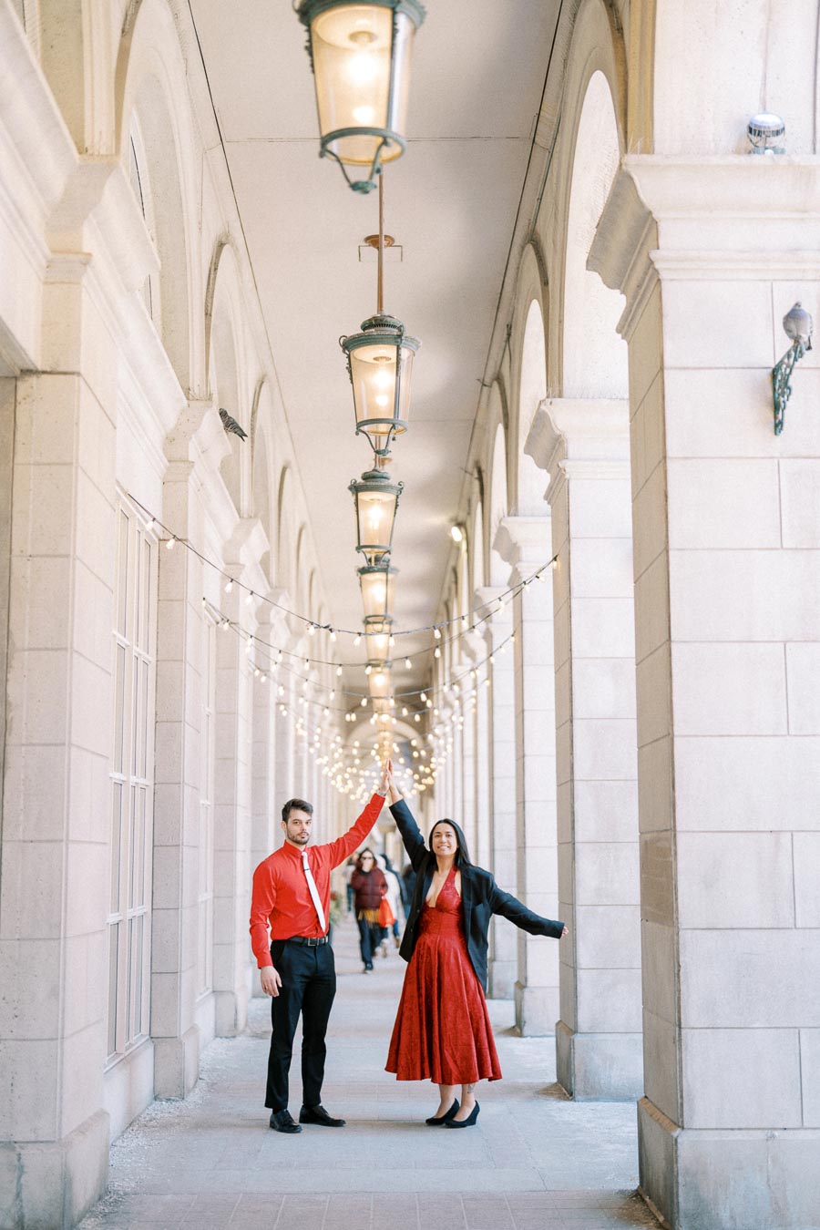 A couple dressed in red stands under a beautifully lit arched walkway, creating a romantic and elegant scene.