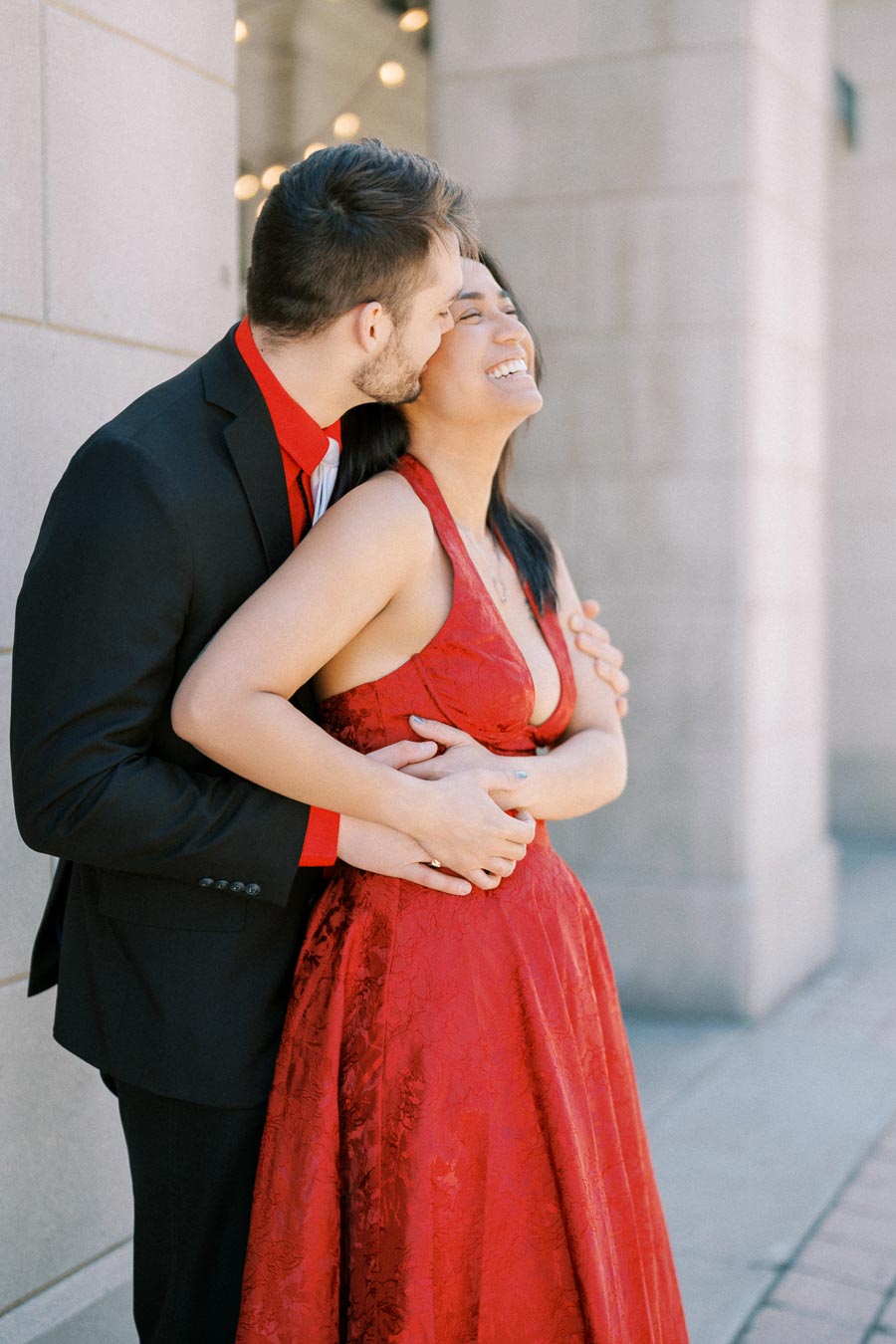 A joyful couple shares a loving embrace, with the woman in a red dress and the man in a black suit.