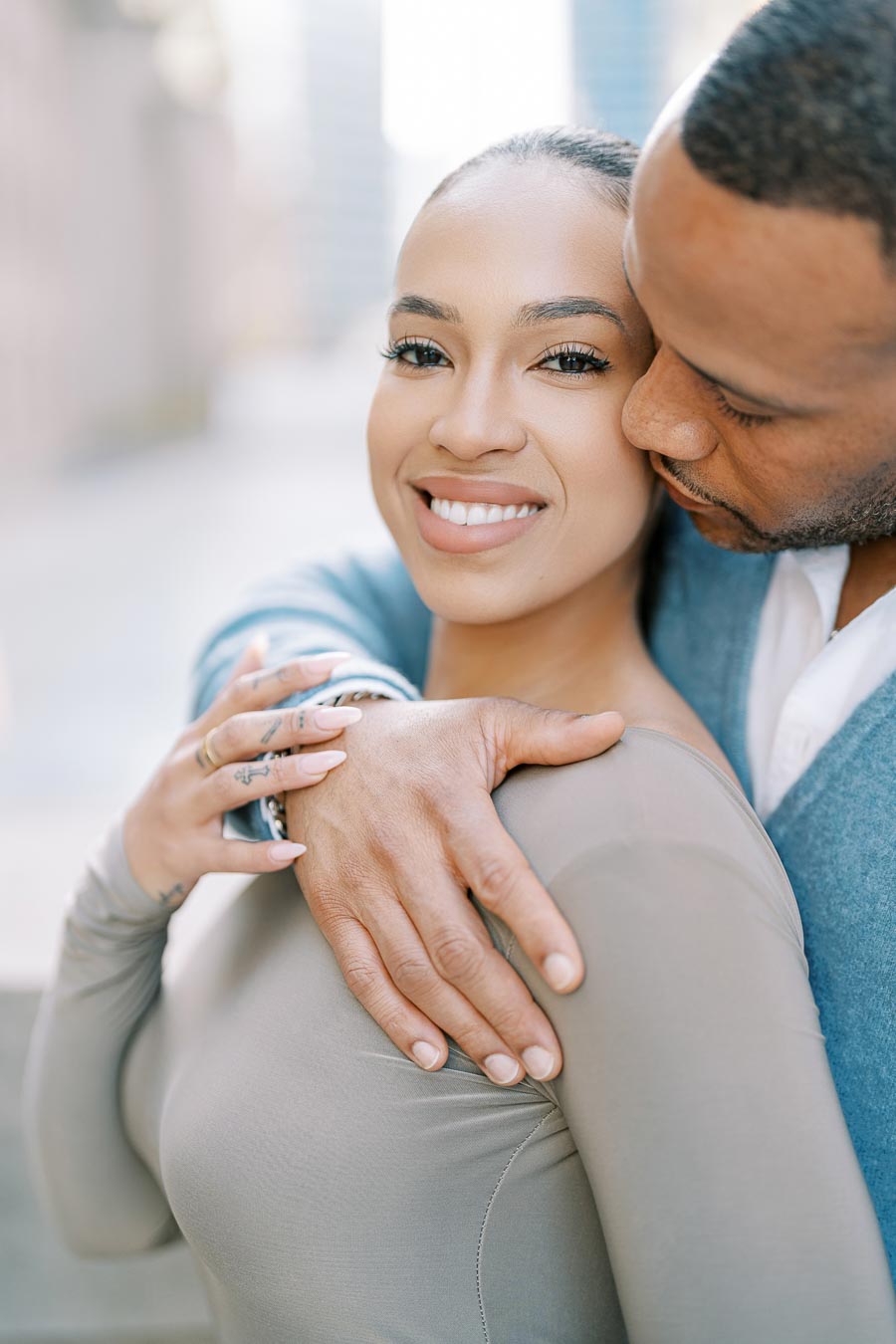 A couple shares a tender moment, with the woman smiling warmly at the camera while the man embraces her lovingly.