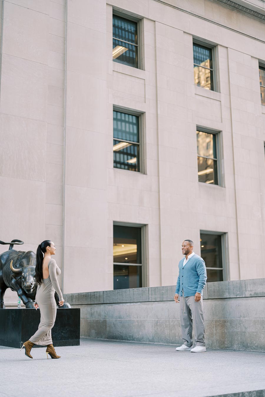 A woman and a man stand near a bull statue in an urban environment, possibly a financial district.