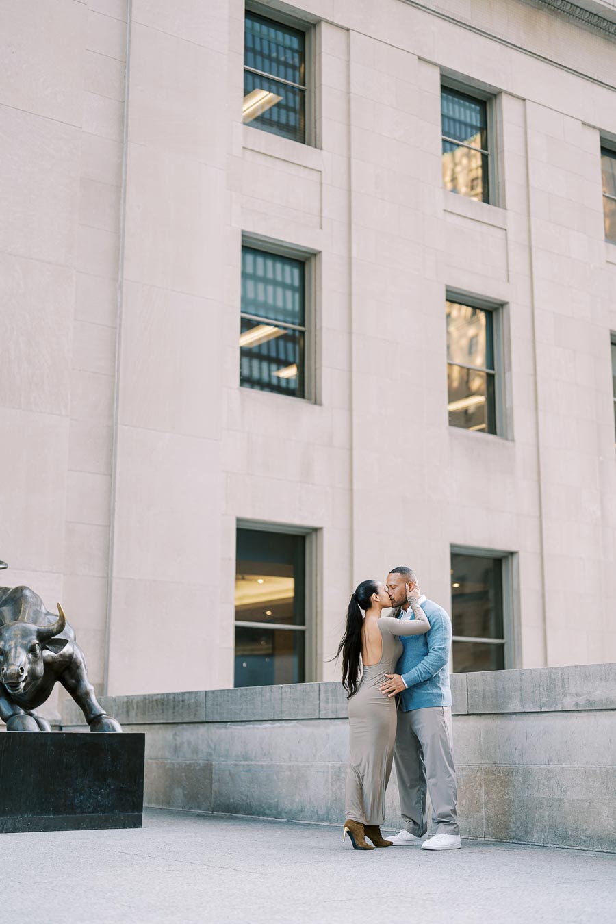 A couple shares a romantic moment in front of a building, with a bull statue visible to the side.