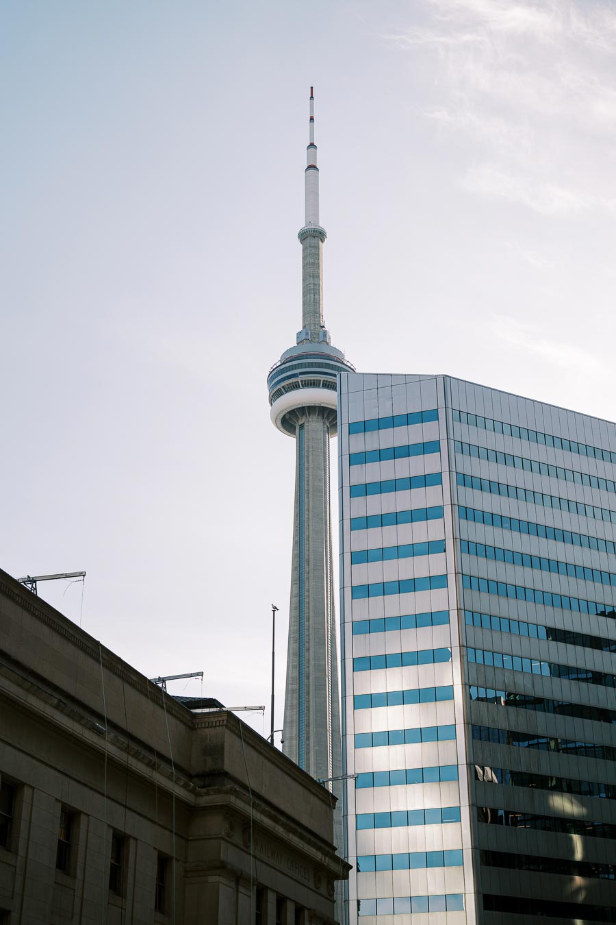 The CN Tower in Toronto, Canada, stands tall against a clear sky, surrounded by modern and historic buildings.