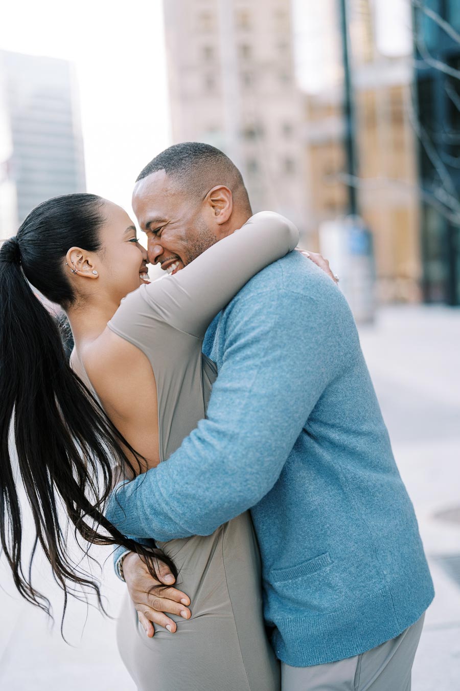 A couple shares a joyful embrace in a city setting, with tall buildings in the background.