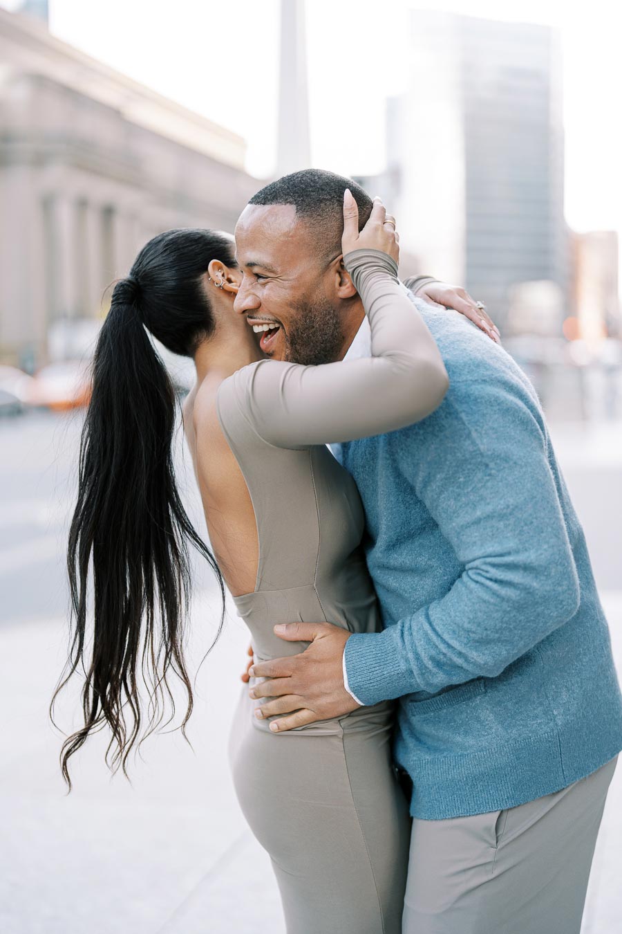 A joyful couple embraces in an urban setting, with a tall building visible in the background, capturing a moment of happiness.