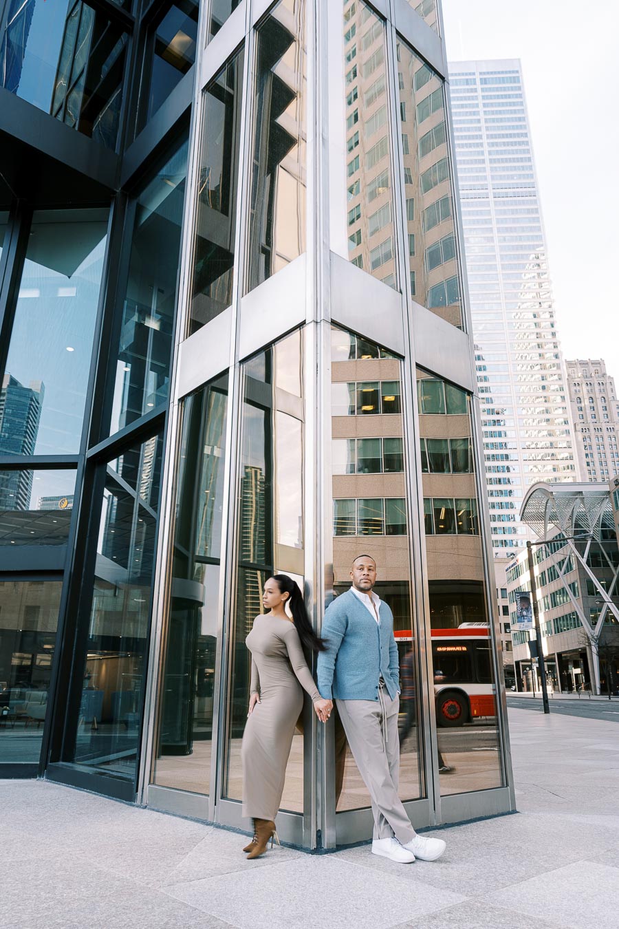 DeVon Franklin and Maria Castillo holding hands on opposite sides of a glass building corner in downtown Toronto during their engagement session