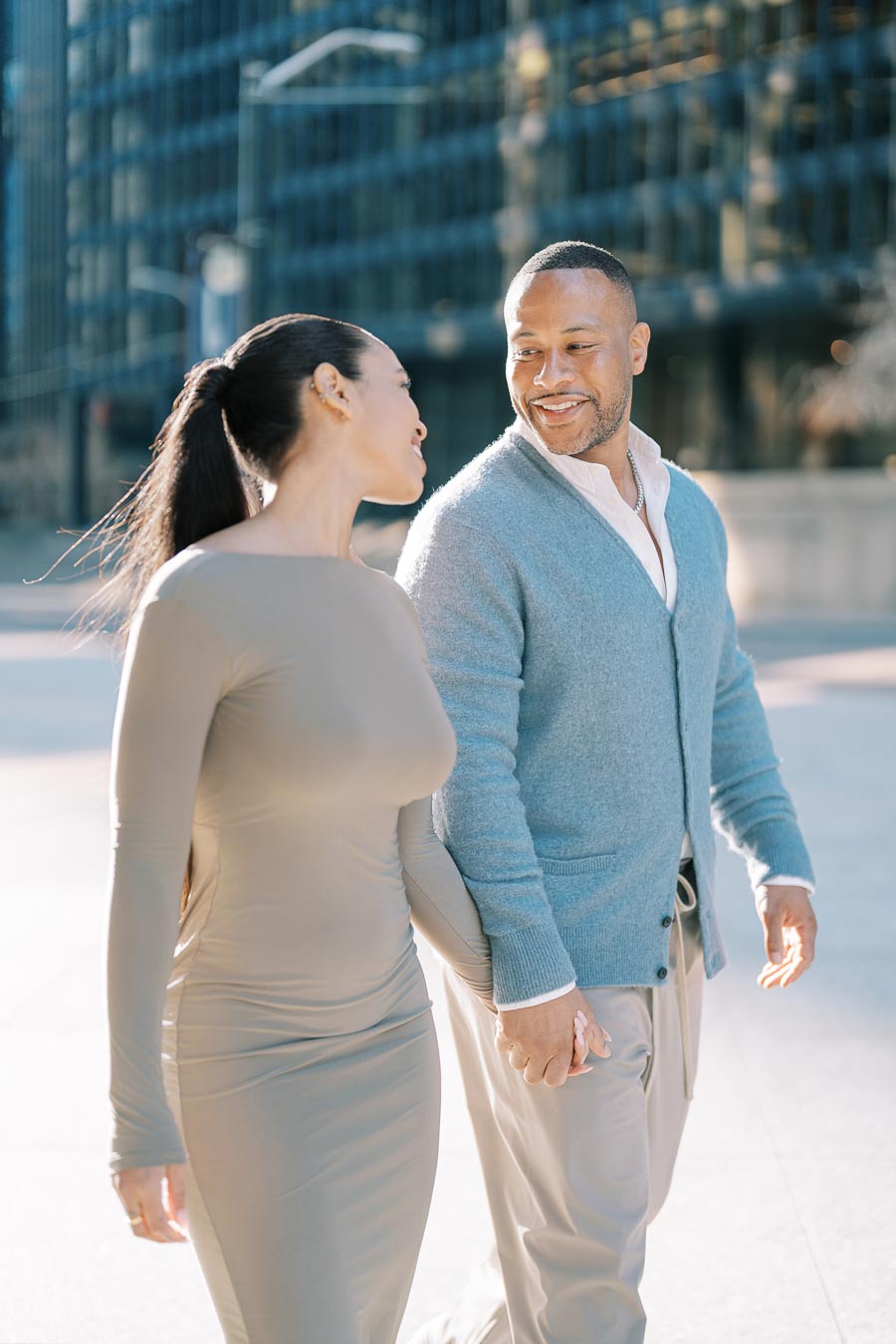 A couple enjoys a sunny day in the city, walking hand in hand and sharing smiles.