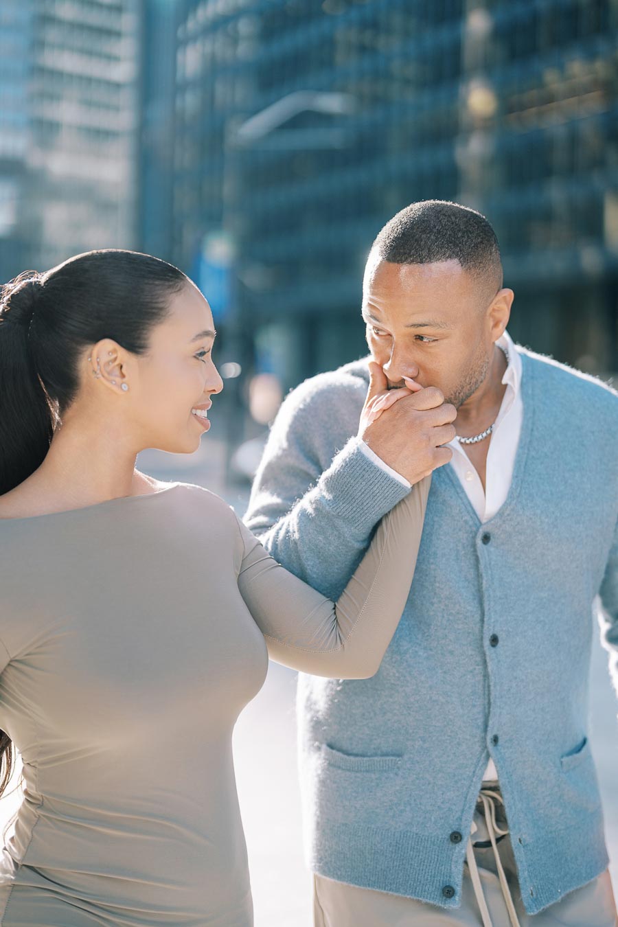 A couple shares a tender moment in an urban setting, with the man kissing the woman's hand.