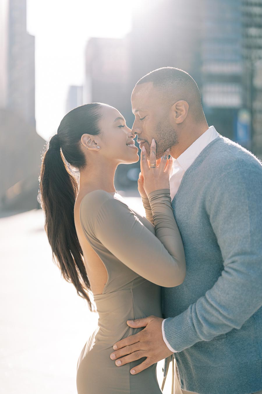 A couple shares a tender moment in an urban setting, with sunlight creating a warm, romantic atmosphere.