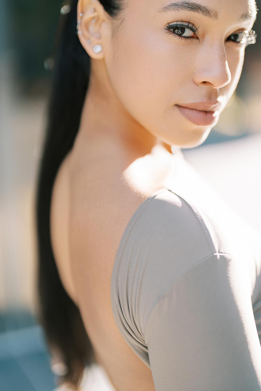A close-up portrait of a woman with long dark hair, showcasing her elegant earrings and light-colored top, as she gazes over her shoulder.
