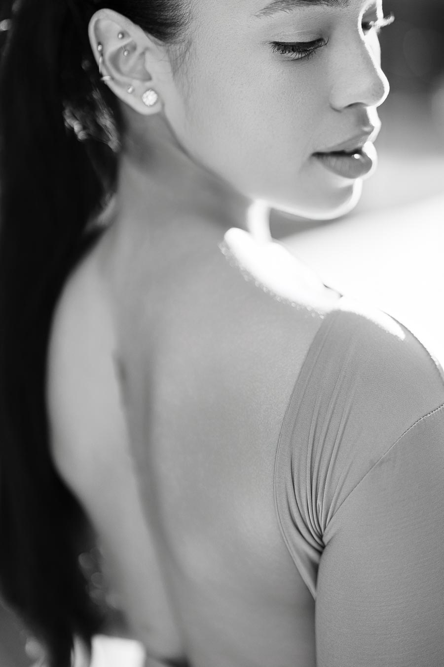 A black and white portrait captures a woman looking over her shoulder, showcasing her earrings and smooth skin.