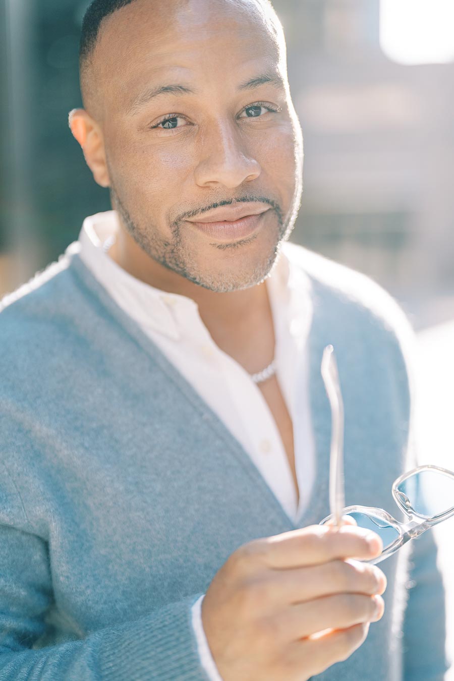 DeVon Franklin smiling and holding eyeglasses during a sunny downtown Toronto engagement photoshoot