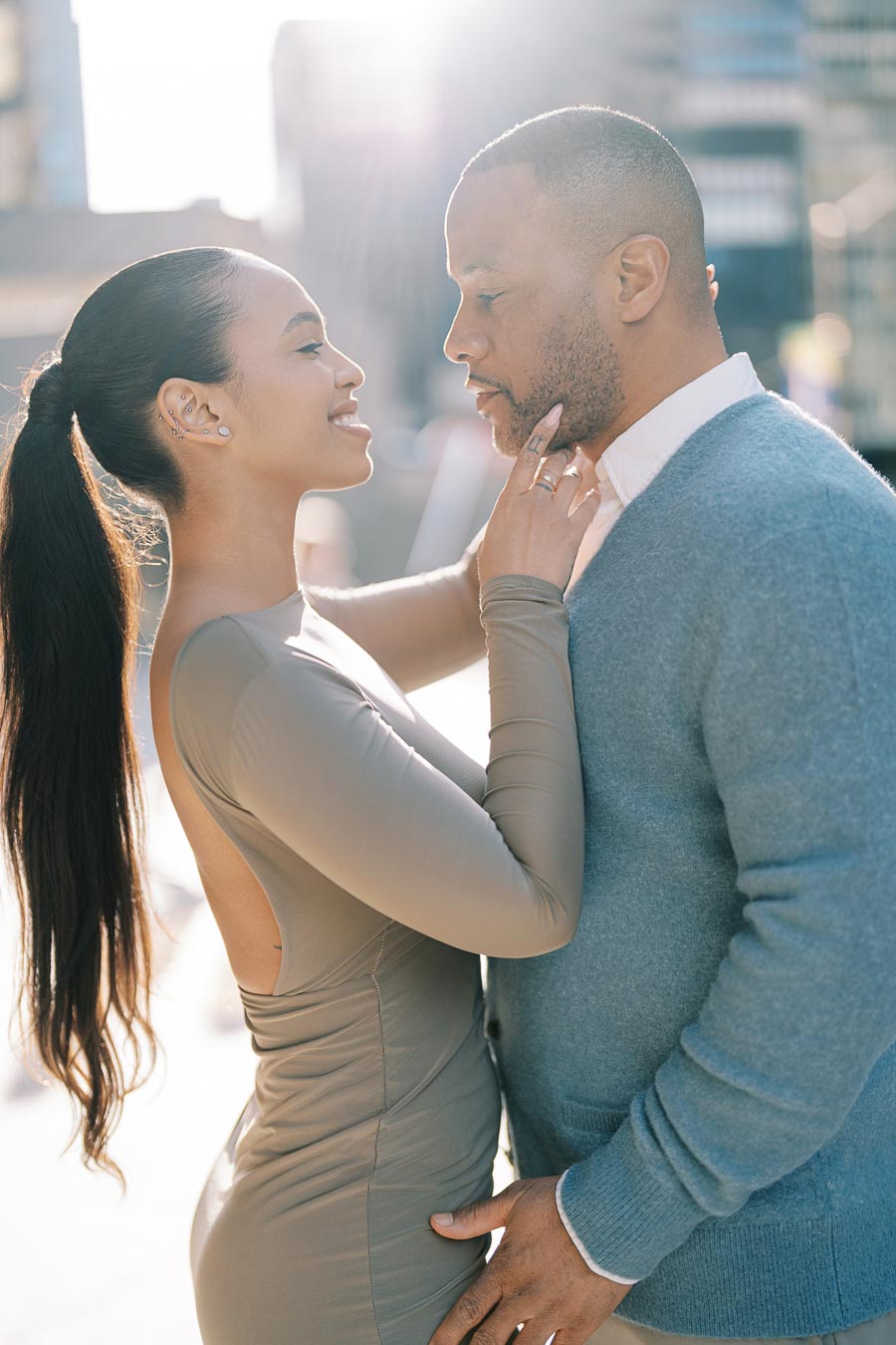 Maria Castillo smiling and gently holding DeVon Franklin’s chin during their golden hour engagement shoot in downtown Toronto