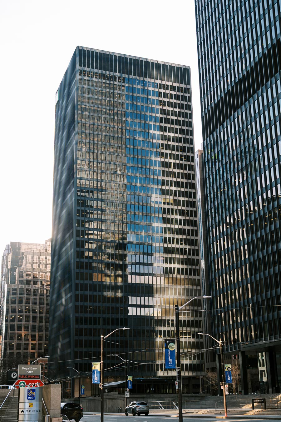 A view of modern skyscrapers with reflective glass windows in an urban city center, featuring the Royal Bank Plaza sign and street banners.