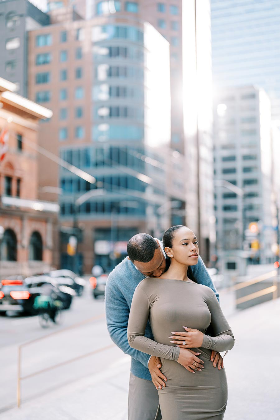 Couple embracing on a downtown Toronto sidewalk with soft sunlight and modern architecture in the background