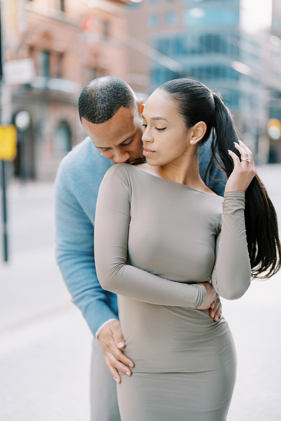 Groom-to-be embracing and kissing fiancée’s shoulder during stylish engagement session in downtown Toronto