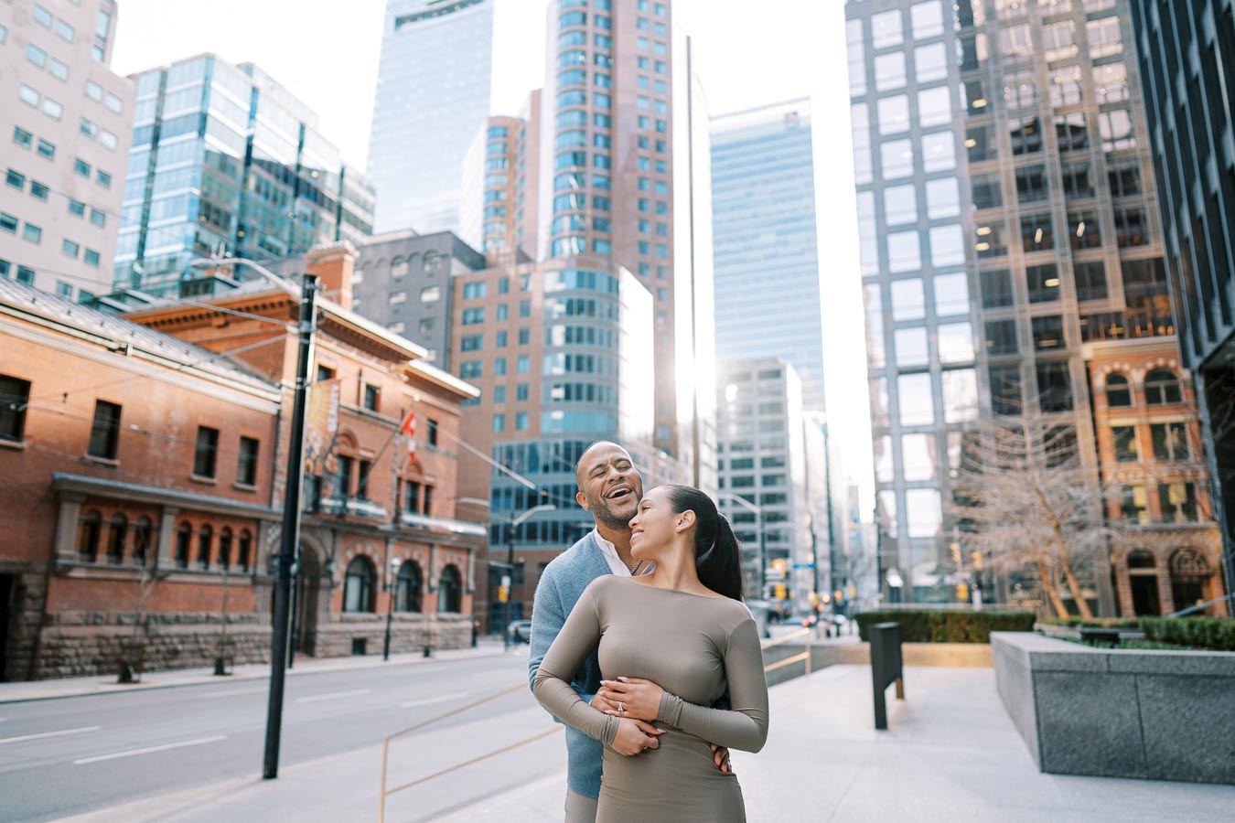 Couple laughing and hugging on a quiet downtown Toronto street surrounded by modern buildings during engagement session