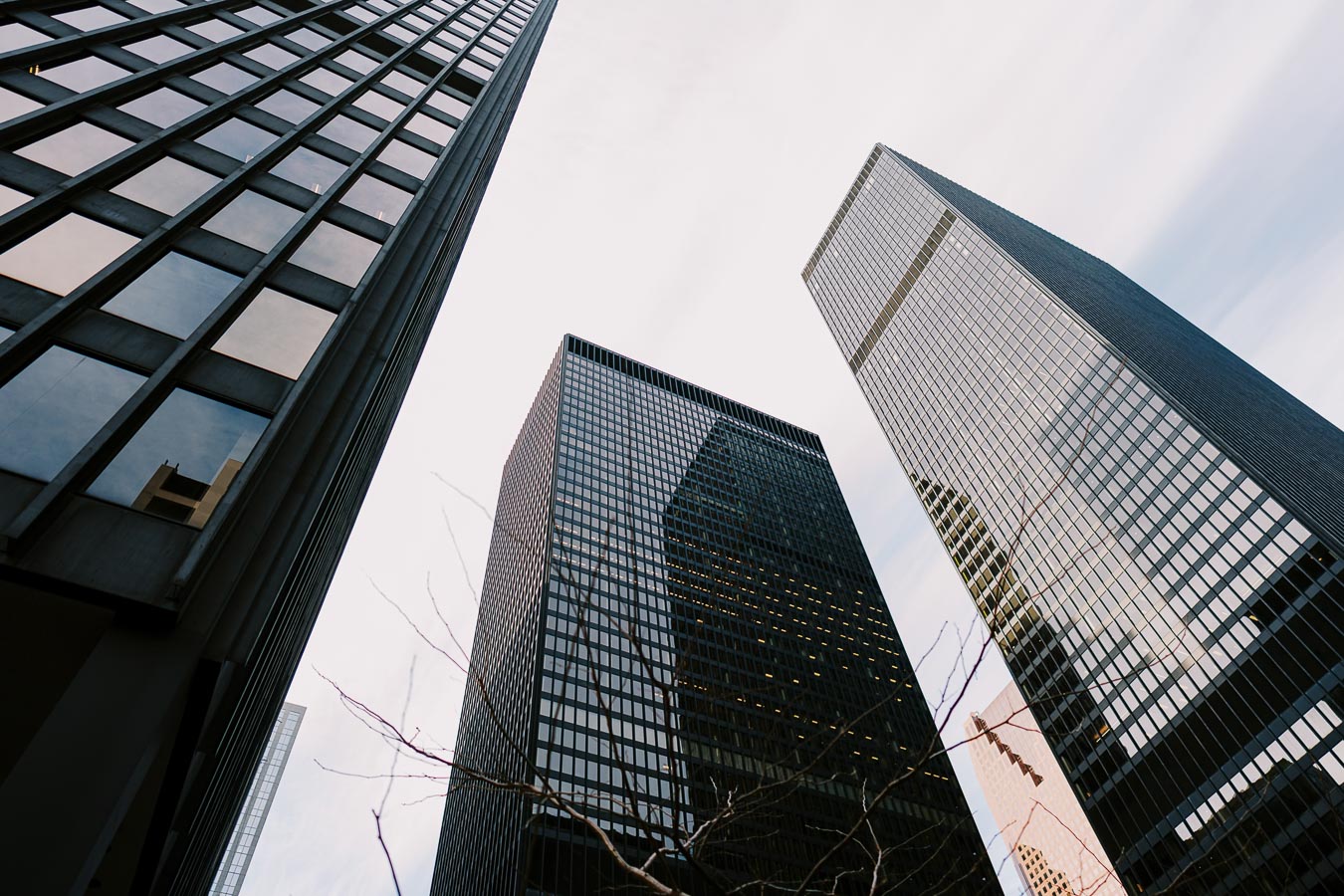 A low-angle view of three modern skyscrapers with glass facades, showcasing their towering presence against a cloudy sky.