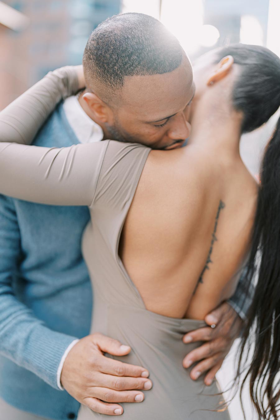 A couple shares an intimate embrace, highlighting the woman's back tattoo and the man's gentle hold.