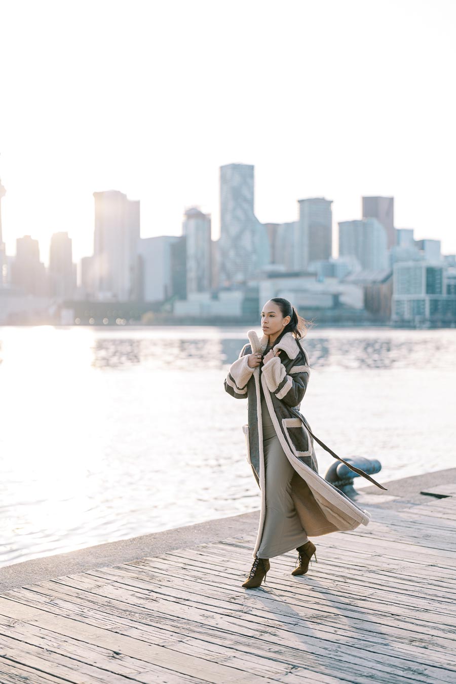 Stylish bride-to-be walking along Toronto waterfront boardwalk with skyline in background during engagement session