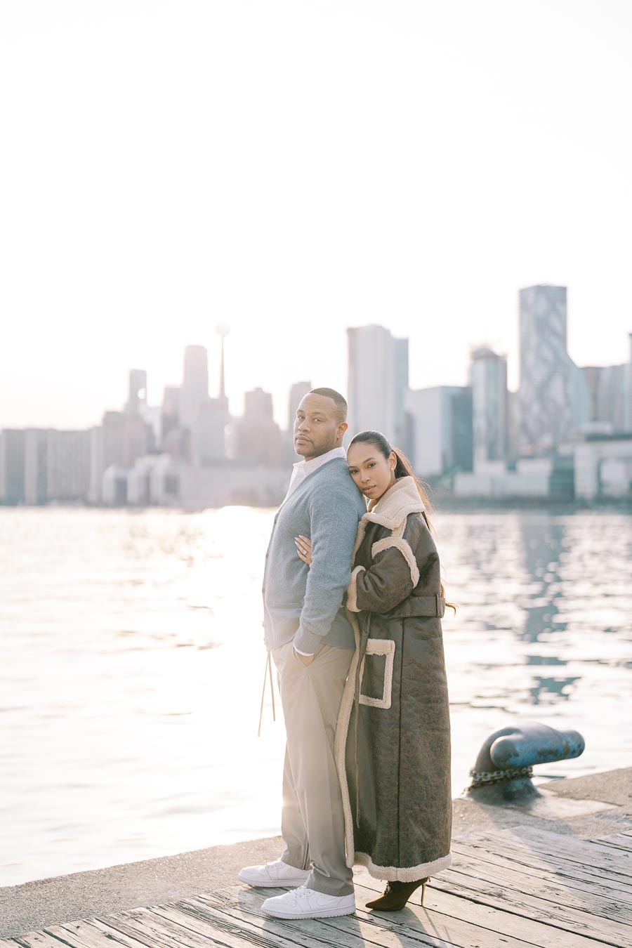 Engaged couple standing on a Toronto pier at sunset, city skyline in the background