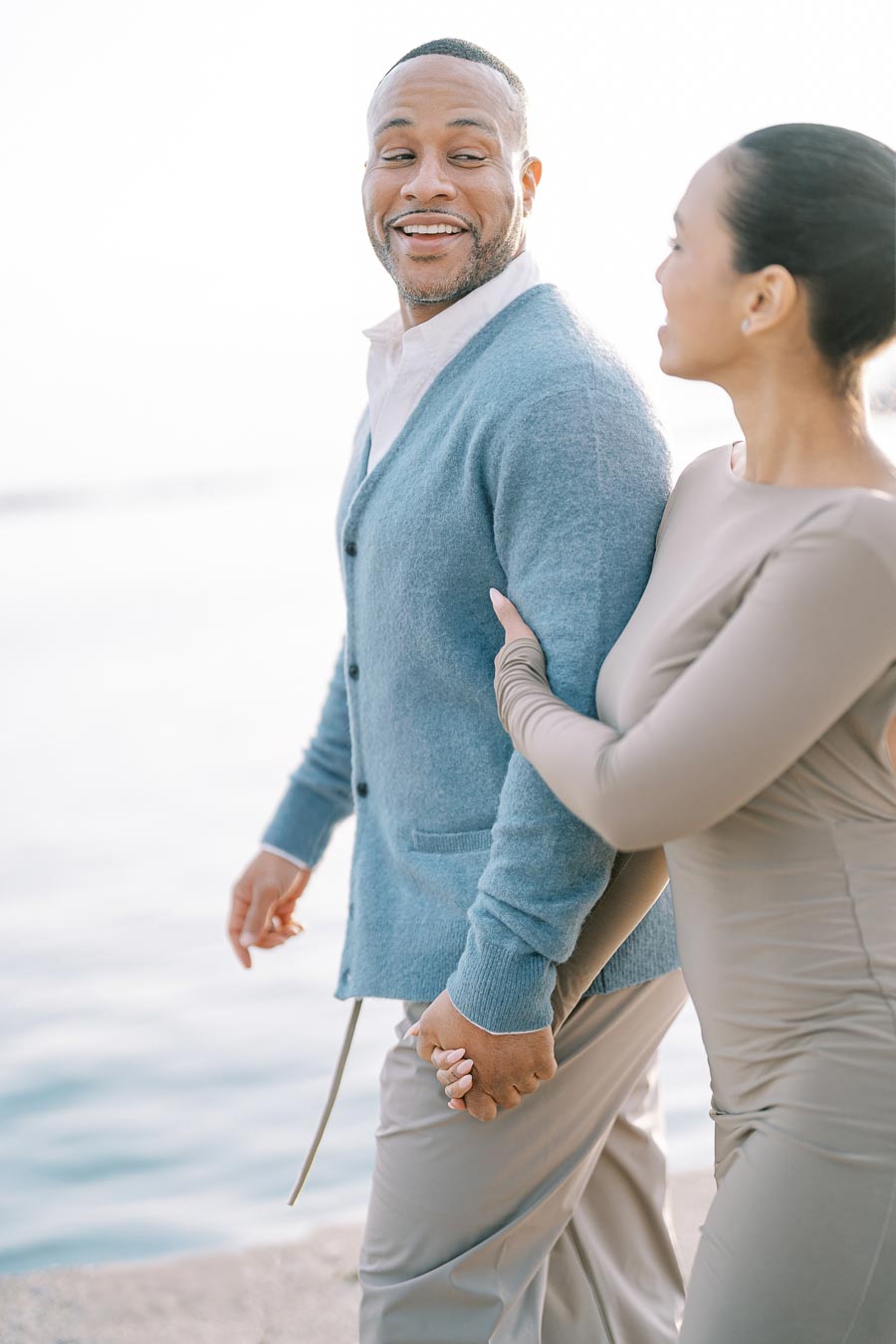 A couple enjoys a walk by the water, holding hands and sharing a smile.