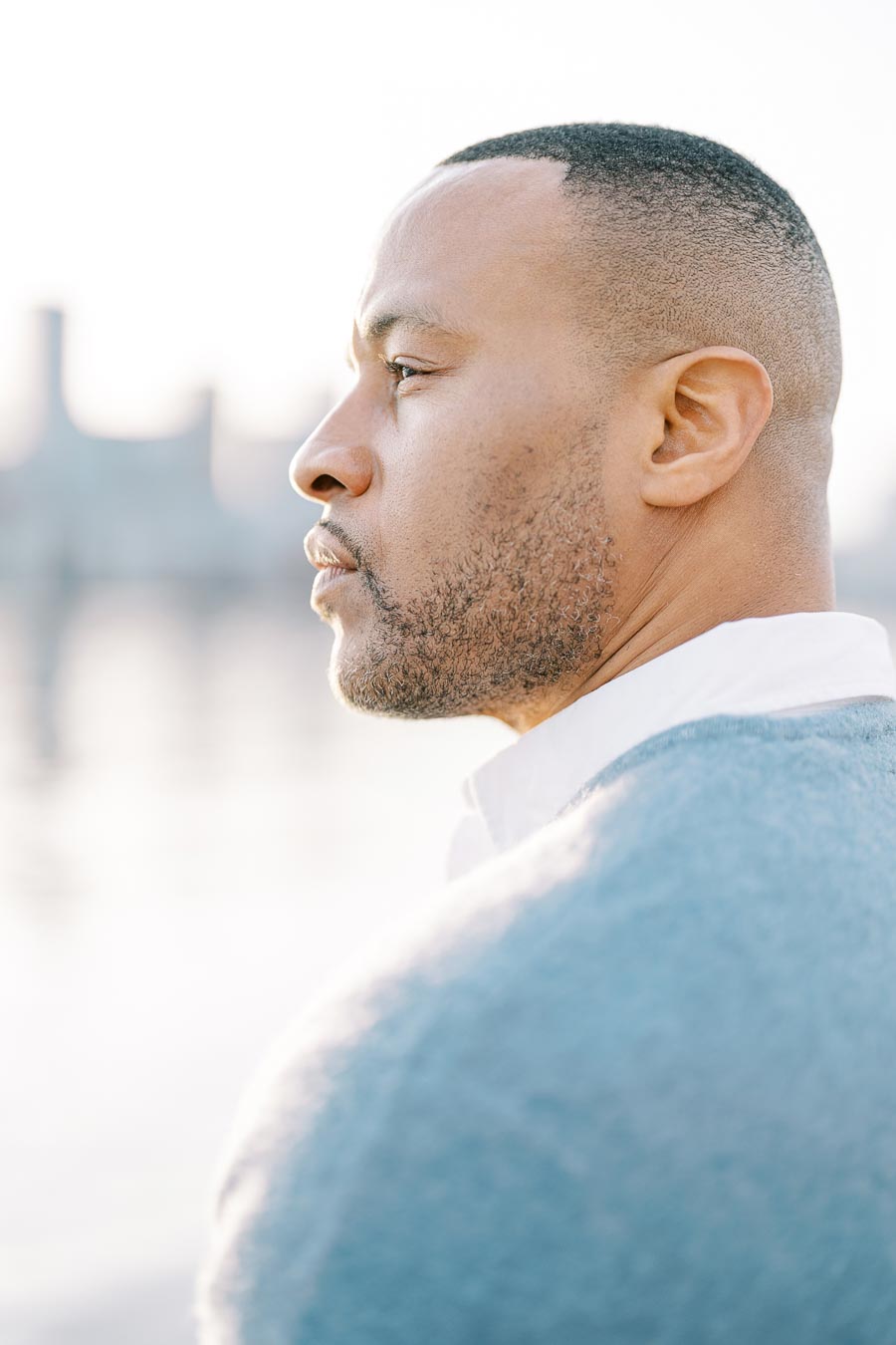 Close-up profile of groom in blue sweater looking thoughtfully across Toronto waterfront