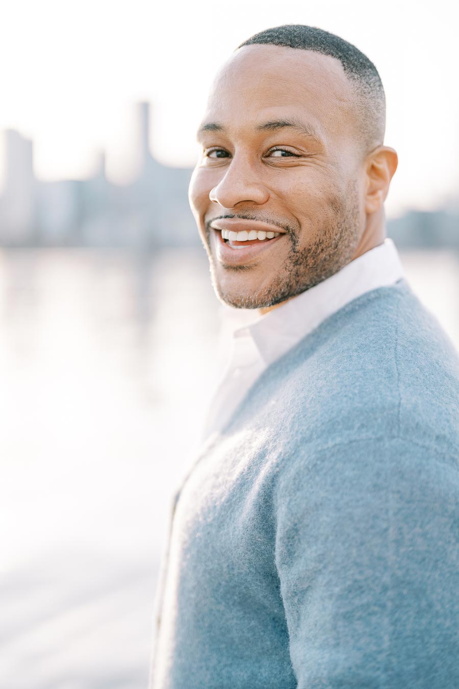 Smiling man in a blue sweater looking over his shoulder during a golden hour photoshoot in Toronto