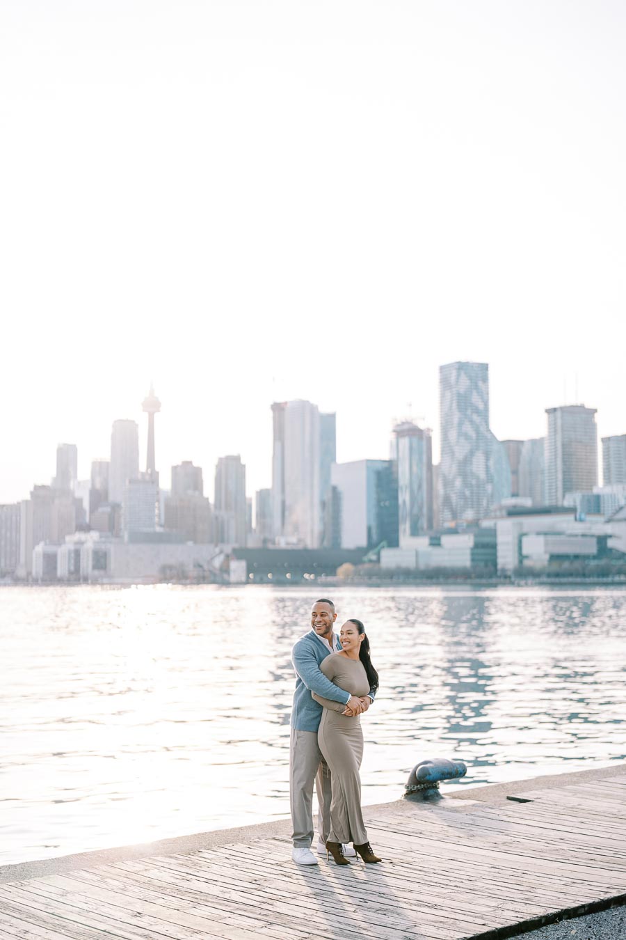 DeVon Franklin and Maria Castillo smiling and embracing at Polson Pier with the Toronto skyline behind them