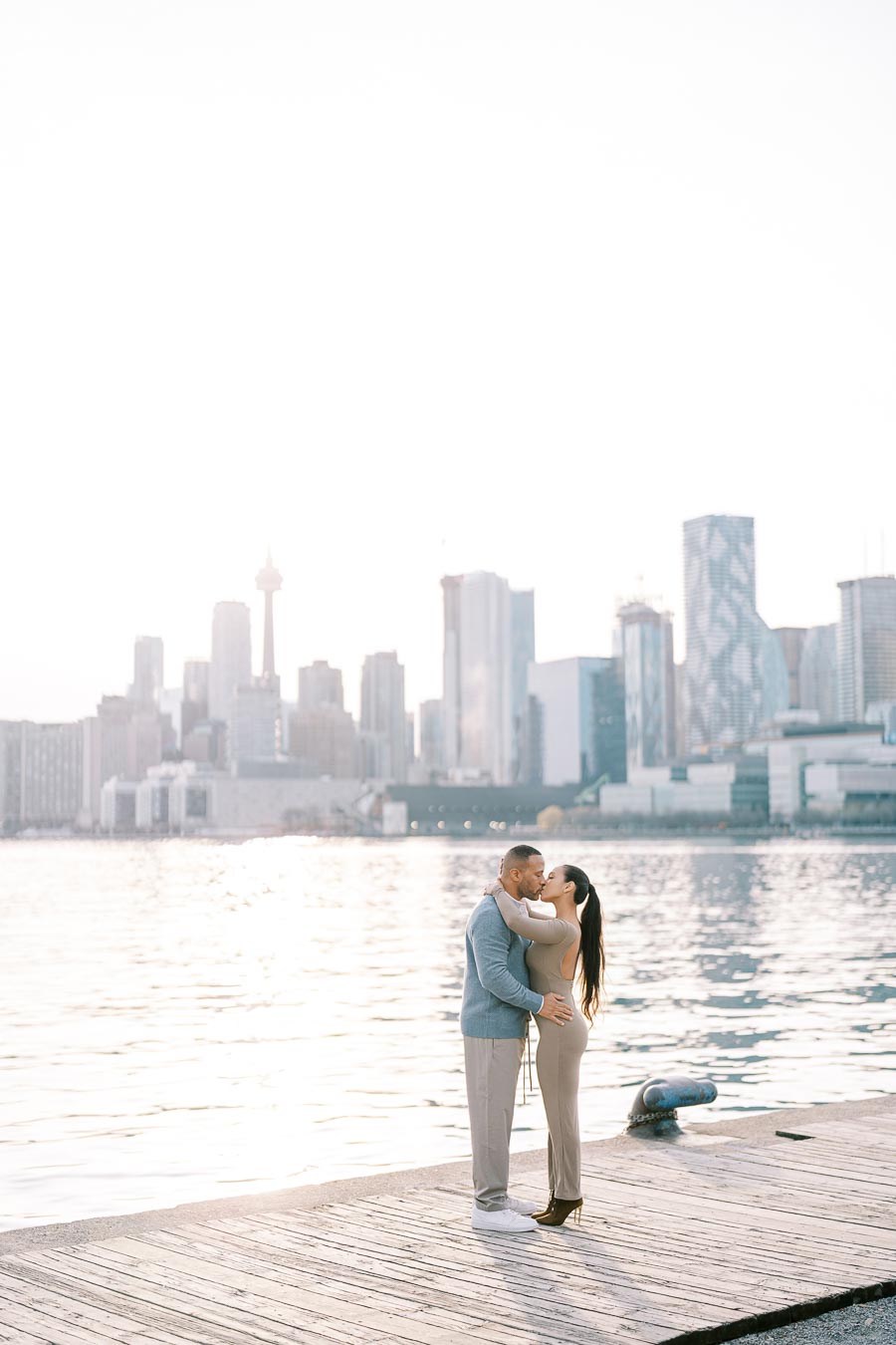DeVon Franklin and Maria Castillo kissing on the dock at Polson Pier with Toronto skyline in the background