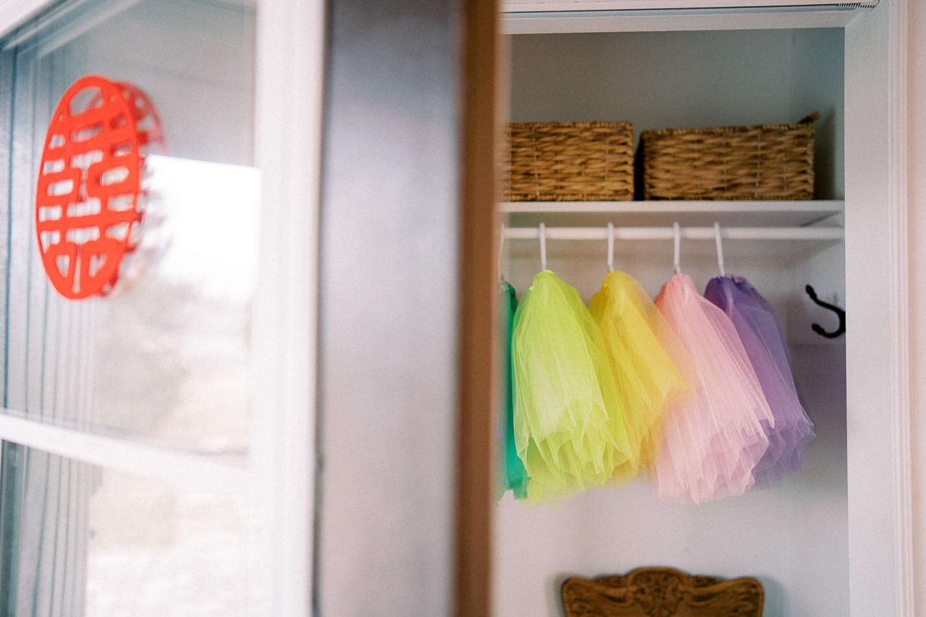 Colorful tutus hanging in a closet with wicker baskets above, showcasing organized wardrobe storage in a bright, modern room.
