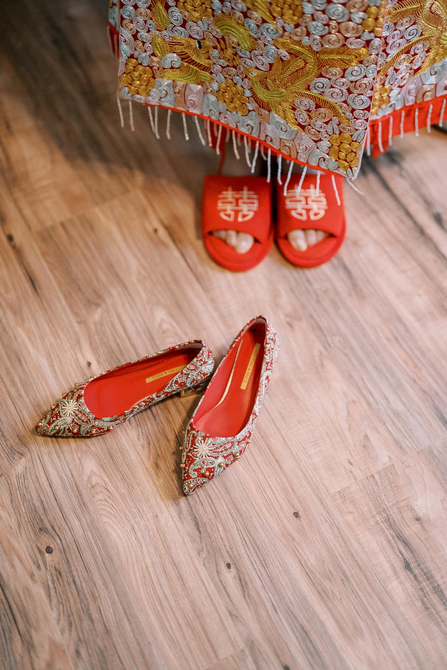 Traditional Chinese wedding attire with intricate embroidery and red embroidered slippers on a wooden floor, symbolizing cultural heritage and celebration.