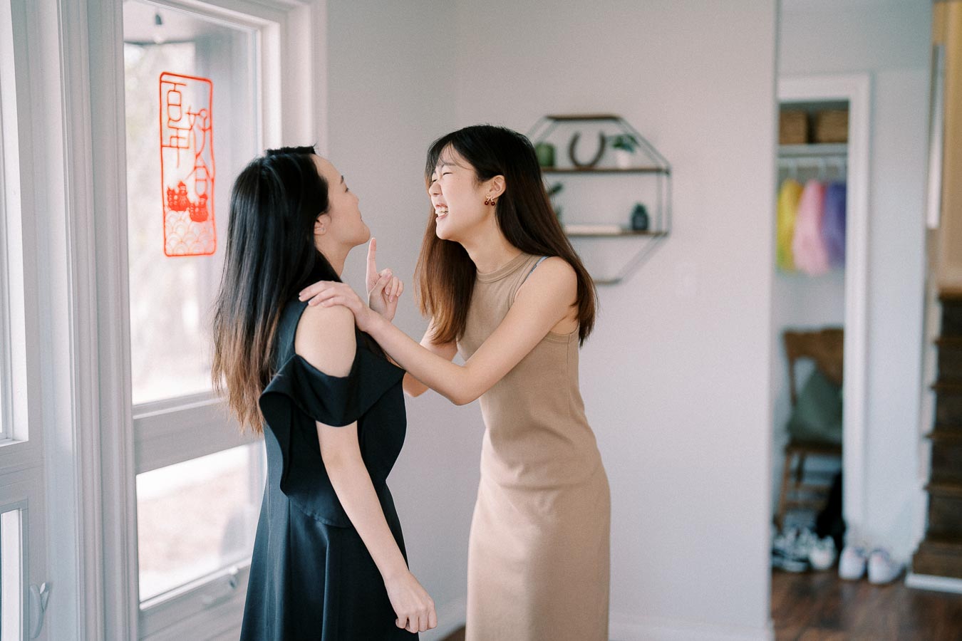 Two women laughing together in a bright, modern living room by the window with decorative artwork.