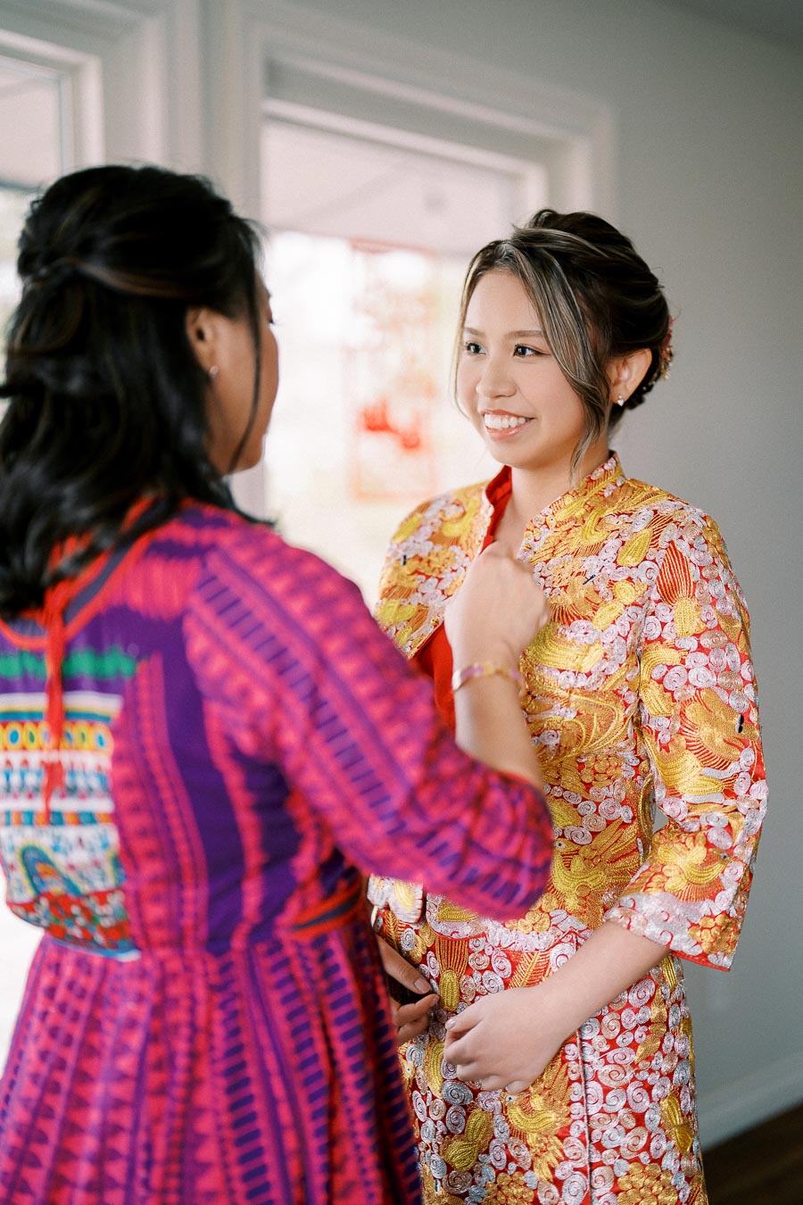 Two women in colorful traditional attire engage in a joyful conversation indoors, highlighting cultural celebration and vibrant fashion.